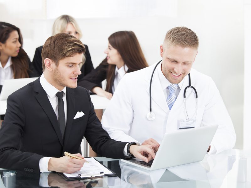 Male doctor and businessman discussing over laptop at desk in office